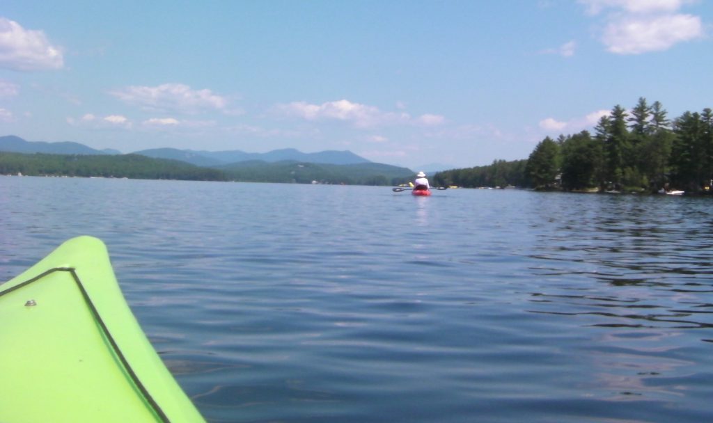 View from inside a kayak paddling across open water, with a red buoy in the distance.